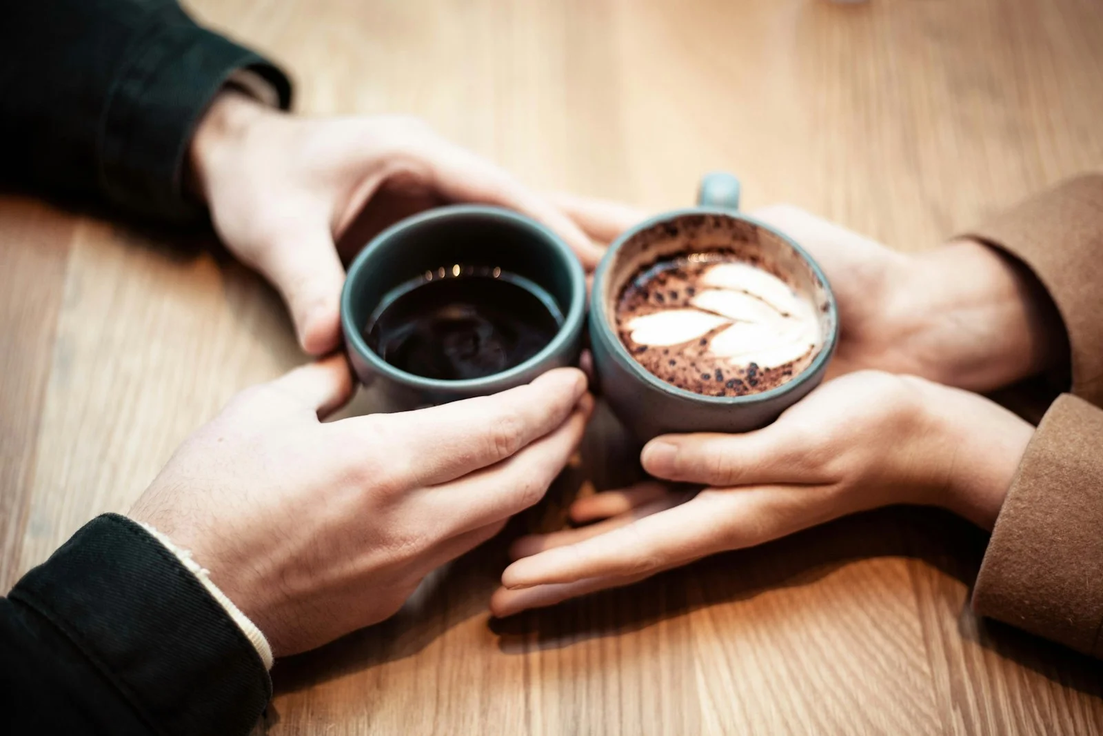 Deux mains qui tiennent des tasses de café sur une table en bois