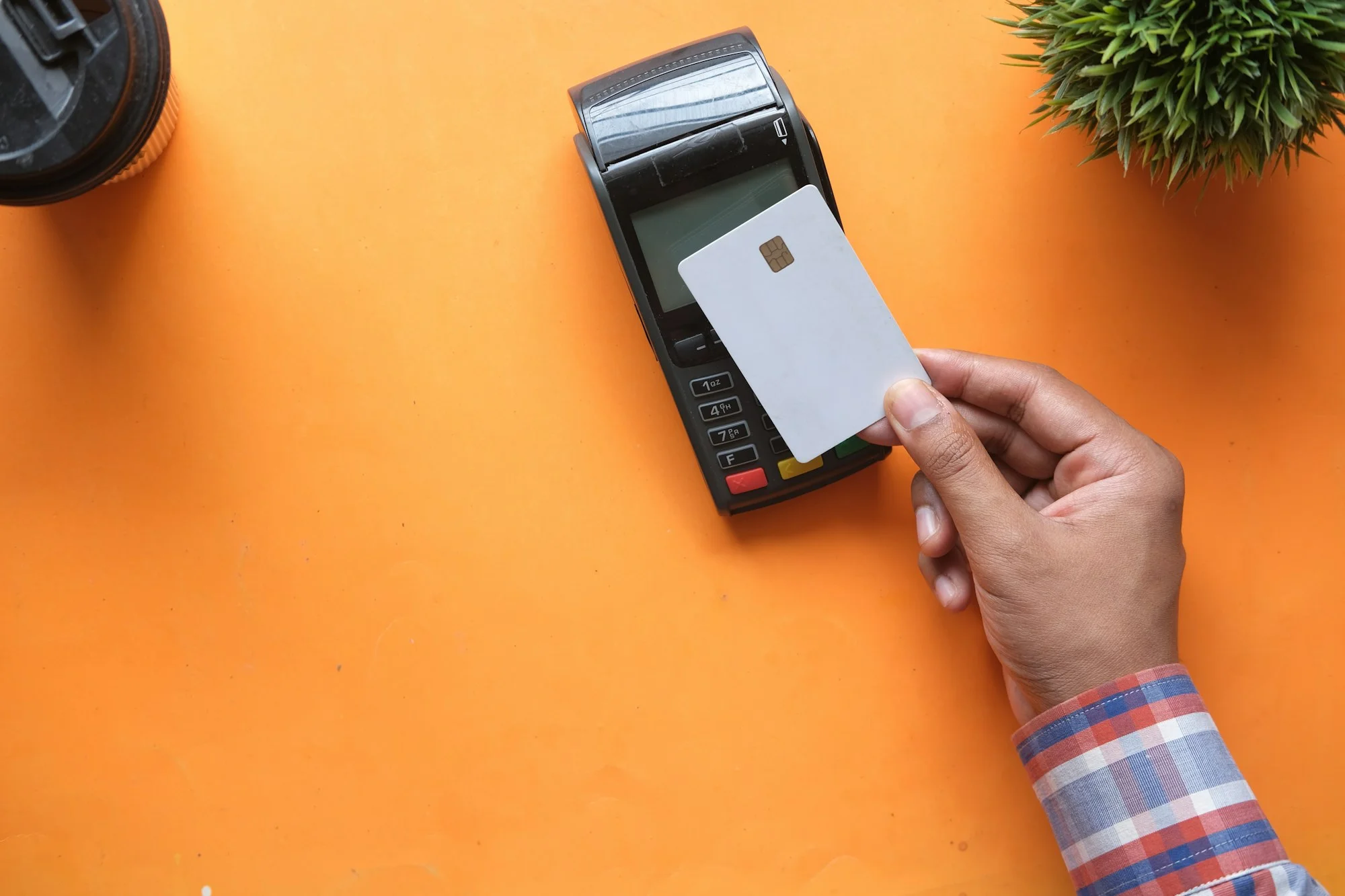 Carte bancaire vierge approchée d’un terminal de paiement, sur fond orange