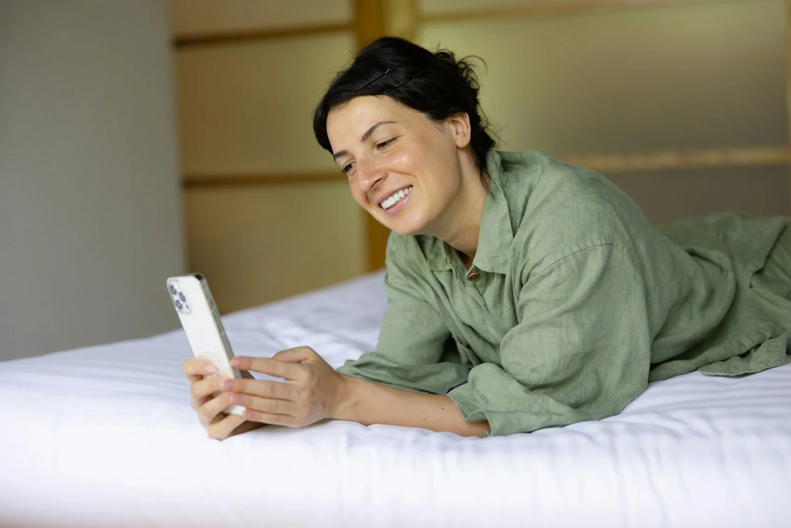 Jeune femme allongée sur un lit qui lit sur son téléphone en souriant