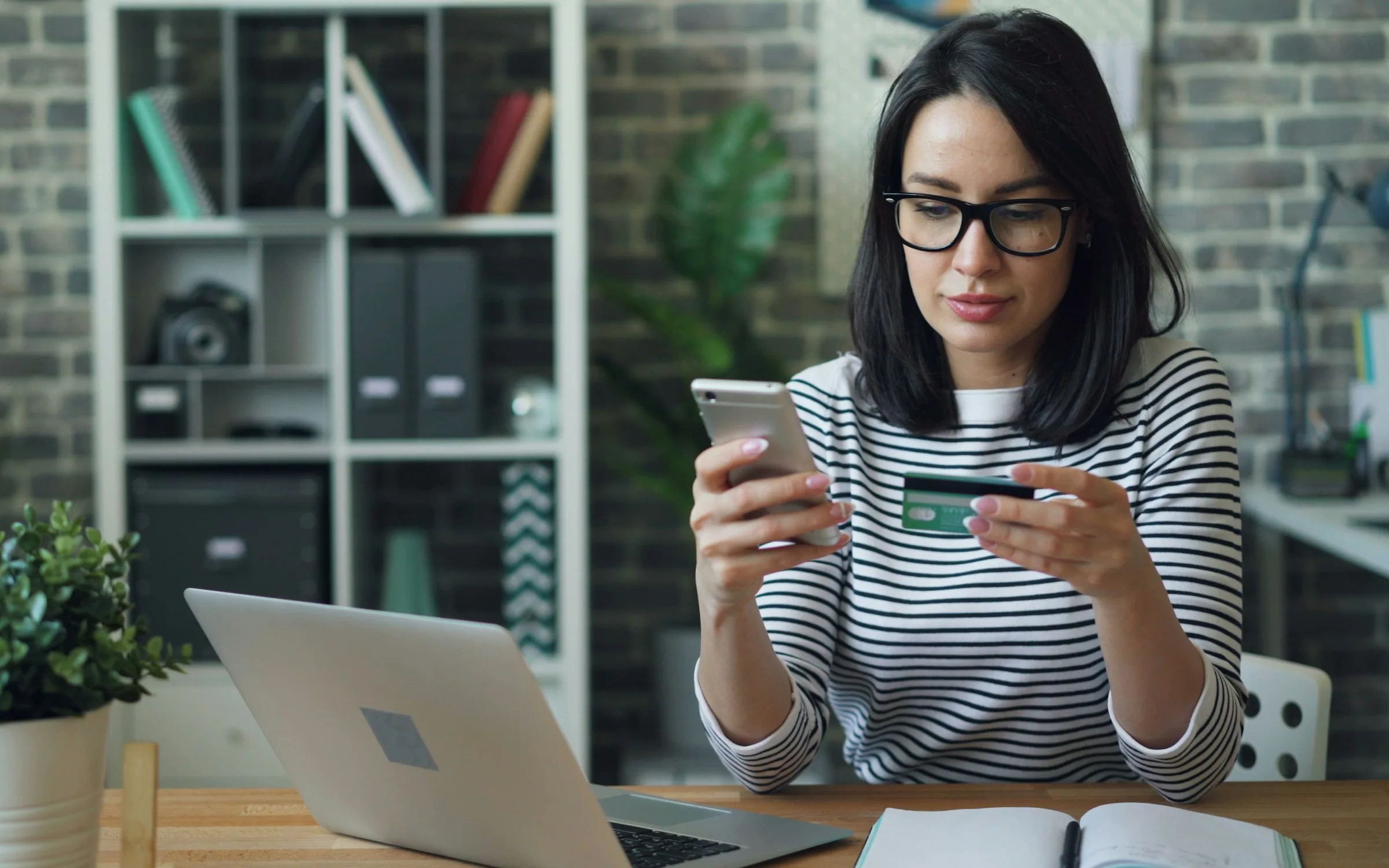 Jeune femme consultant son téléphone, une carte bancaire à la main